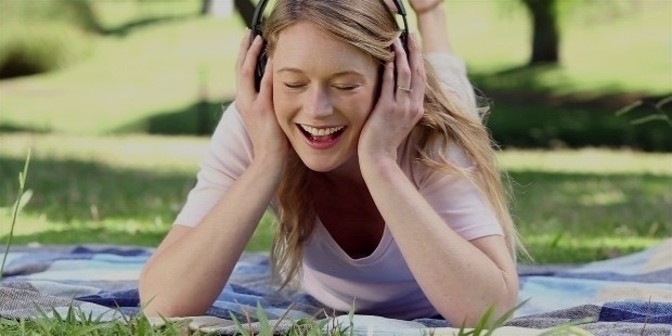 happy girl lying on blanket listening to music in the park on a sunny day